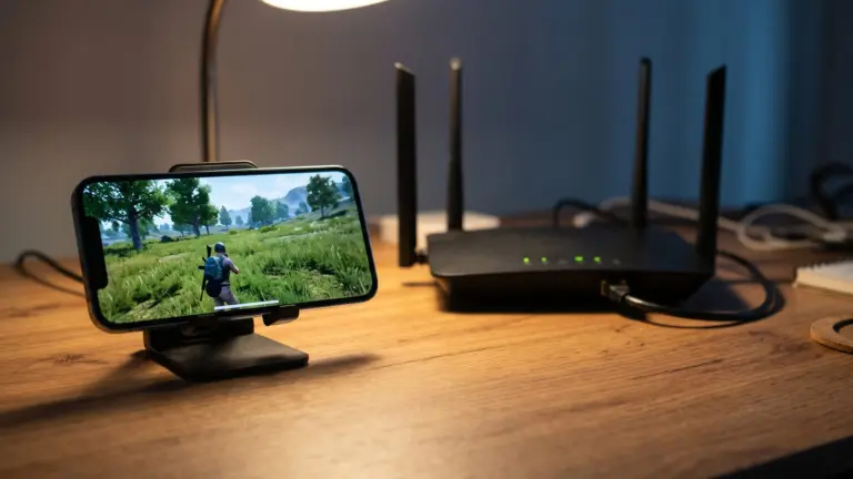 Smartphone running a battle royale game on a desk stand next to a Wi-Fi router with four antennas