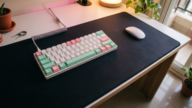 Compact 60 percent white keyboard with pastel keycaps and a mouse on a white desk seen from above