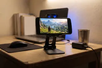 Budget Android phone on a stand with a small cooling fan clipped to its back on a plain study table