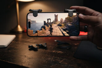 Smartphone with two metal shoulder triggers clipped to its top edge on a wooden desk, spare triggers beside it