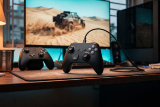 Black wired PC gamepad in front of a gaming monitor and tower PC on a bedroom desk at dusk