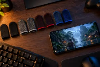 Row of knitted gaming finger sleeves in four colours beside a phone on a wooden desk at night