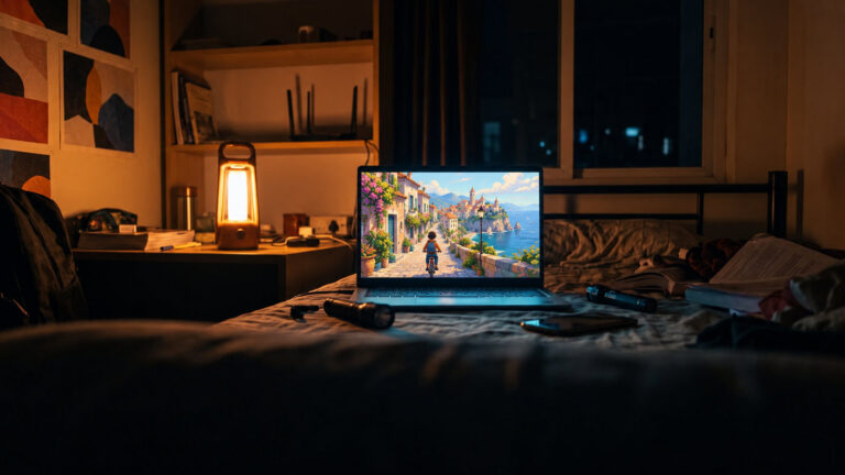 Laptop on a hostel bed during a power cut showing a hand painted seaside town game, lit by an emergency lamp