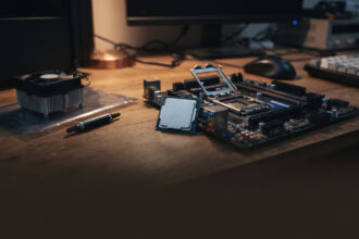 Bare desktop processor chip beside an open motherboard socket with a small stock cooler nearby