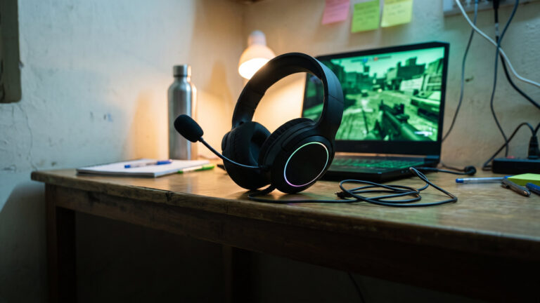 Budget wired plastic gaming headset with boom mic on a hostel study table beside a laptop at night