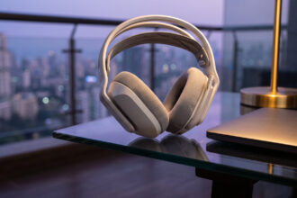 Lightweight white wireless gaming headset on a glass desk in a balcony nook with city lights at dusk