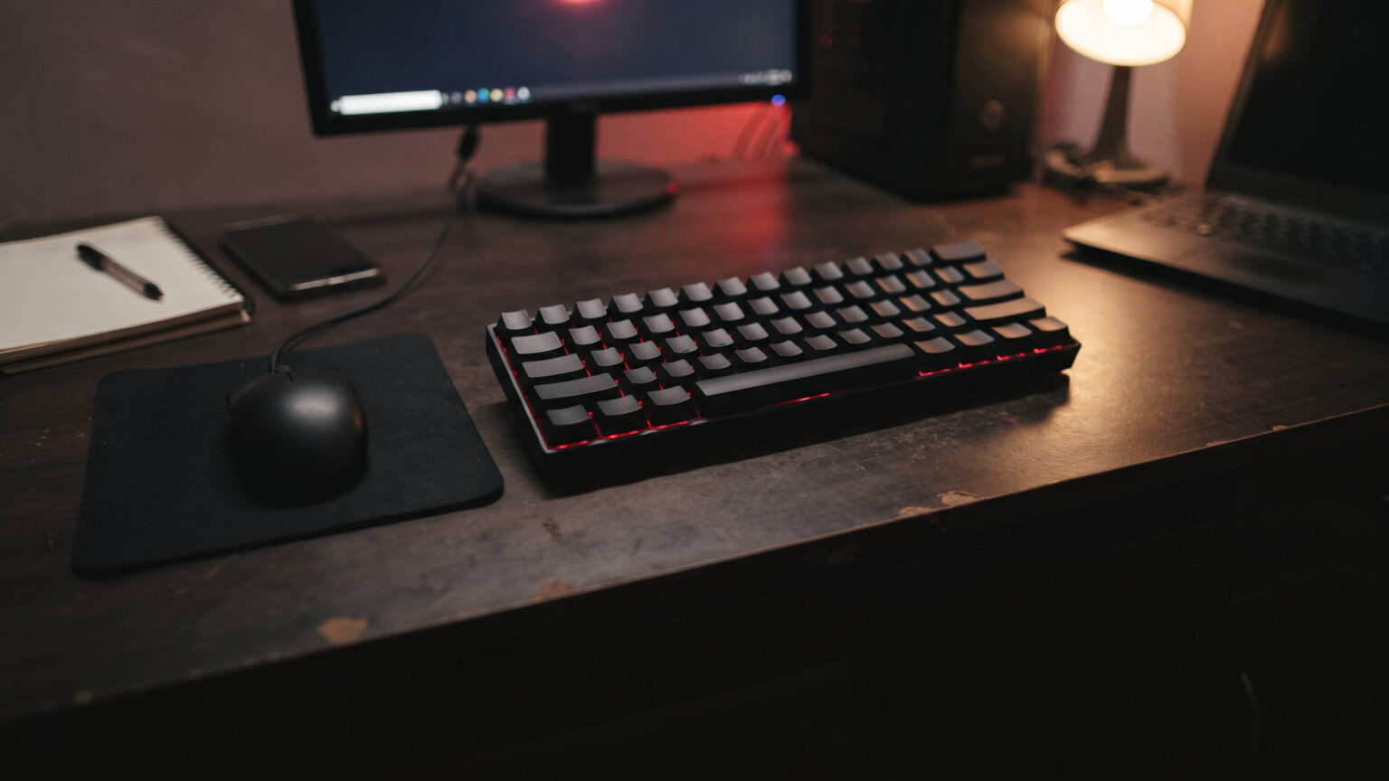Compact black 60 percent keyboard with a red backlight beside a wired mouse on a student desk