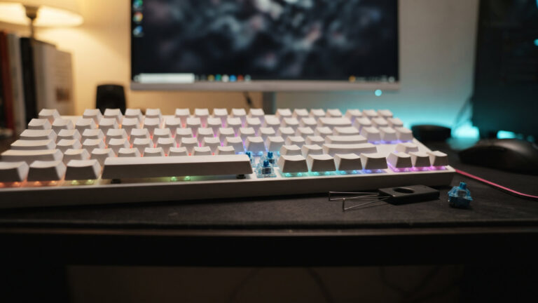 White mechanical keyboard with one keycap removed to show a blue switch, a keycap puller beside it