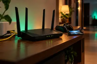 Black four antenna home router with green status lights and a yellow ethernet cable on a shelf at night