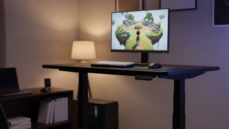 Black electric standing desk raised to standing height with a monitor on top and an empty chair