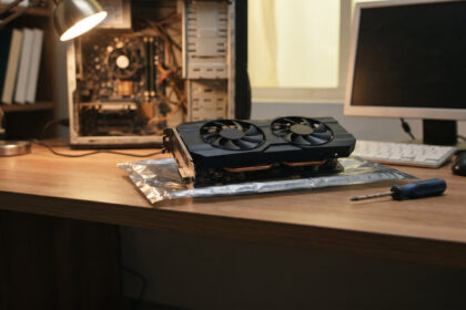 Older dual fan graphics card on an anti static bag beside an open budget PC tower