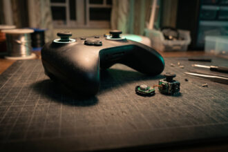Macro of a gamepad thumbstick beside an opened stick module with a small magnet on a repair mat