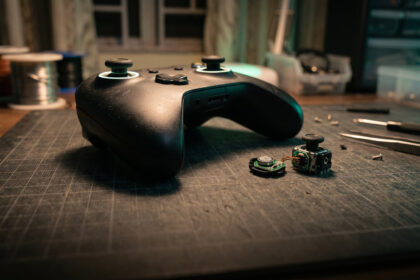 Macro of a gamepad thumbstick beside an opened stick module with a small magnet on a repair mat