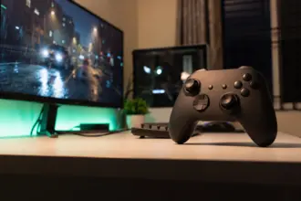 Matte black wireless gamepad on a stand beside an ultrawide monitor on a white desk at night