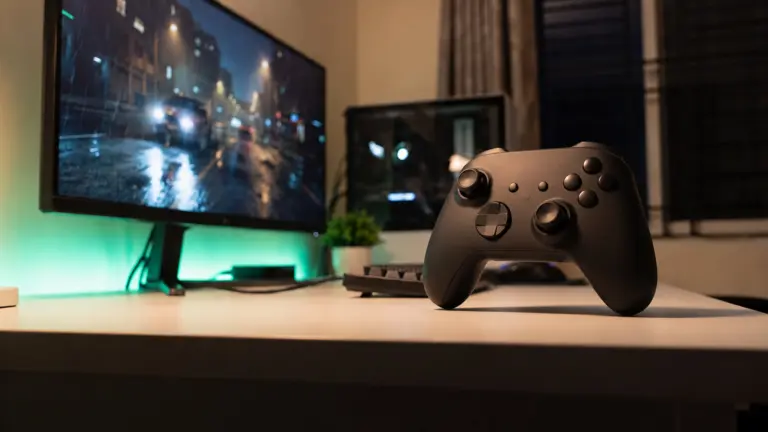 Matte black wireless gamepad on a stand beside an ultrawide monitor on a white desk at night