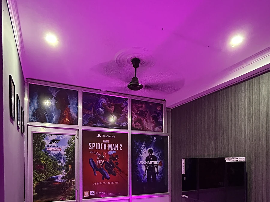 A console room with bean bags, a TV and game posters under purple lighting at Gamer's Adda